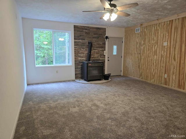 unfurnished living room with carpet flooring, ceiling fan, a wood stove, and a textured ceiling