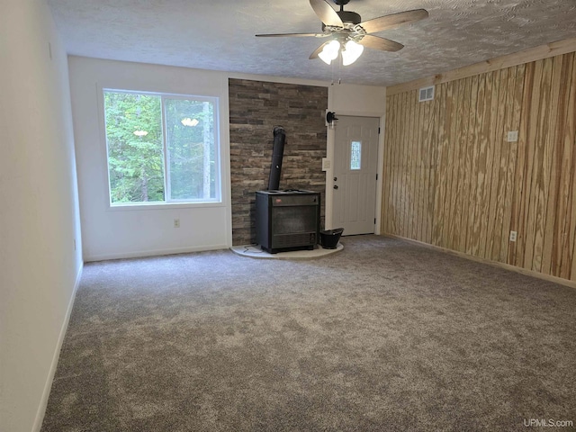 unfurnished living room with a wood stove, carpet flooring, wood walls, and a textured ceiling