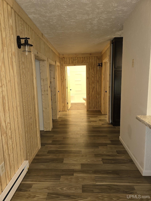 hall with dark wood-style floors, a baseboard radiator, wooden walls, a textured ceiling, and baseboards