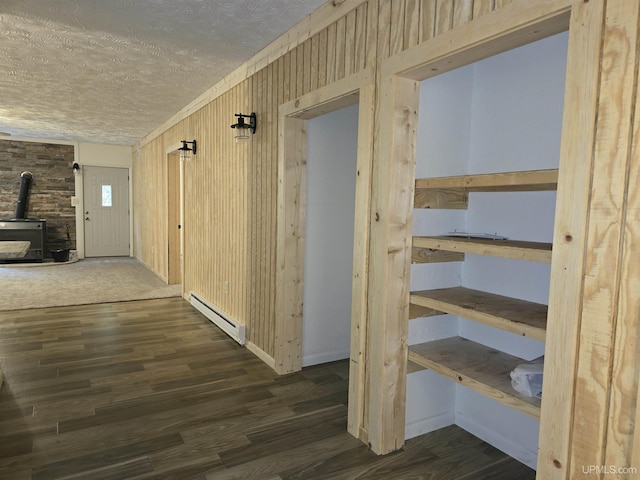 corridor with a textured ceiling, wood walls, baseboard heating, and wood finished floors