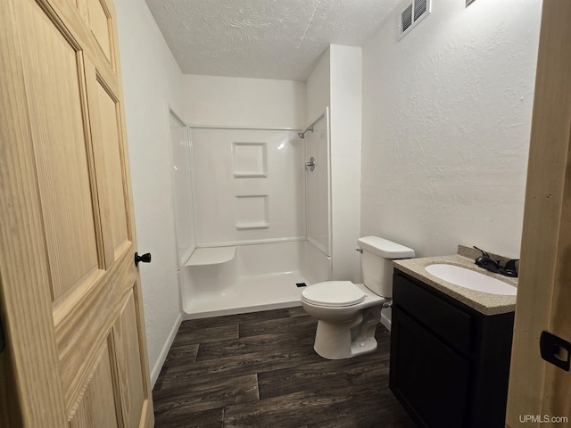 bathroom featuring toilet, wood finished floors, walk in shower, a textured ceiling, and vanity