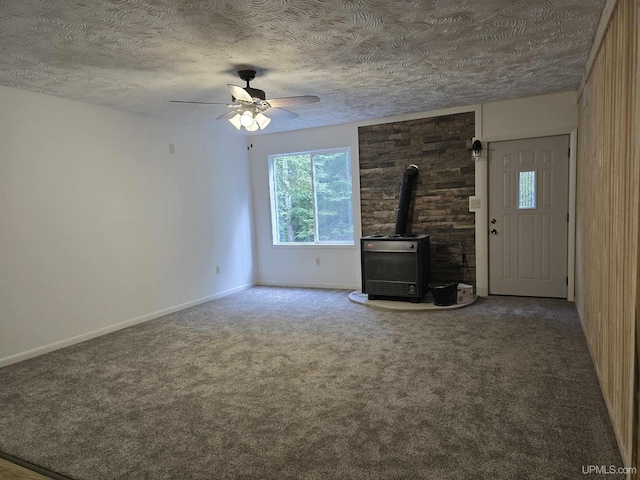 unfurnished living room with baseboards, ceiling fan, a wood stove, a textured ceiling, and carpet flooring