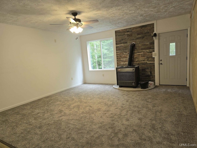 unfurnished living room featuring carpet floors, a wood stove, a textured ceiling, and baseboards