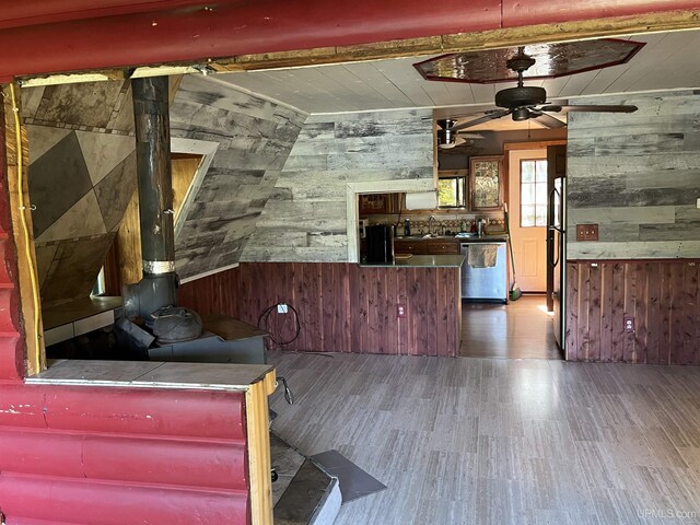 unfurnished living room with ceiling fan, vaulted ceiling, wooden walls, and dark wood-type flooring