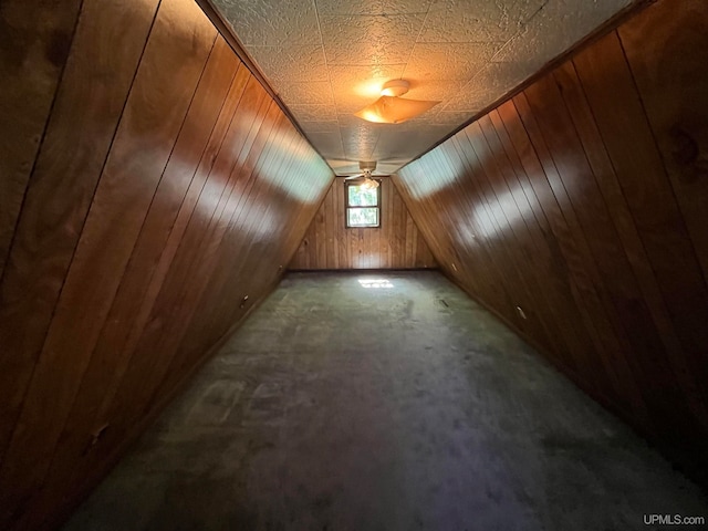 additional living space with dark colored carpet, a textured ceiling, vaulted ceiling, wooden walls, and ceiling fan