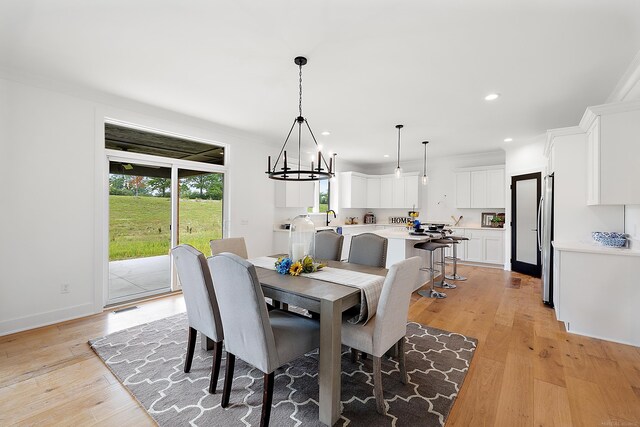 dining area featuring sink, light wood-type flooring, a notable chandelier, and a healthy amount of sunlight