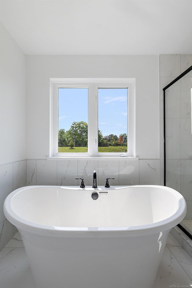 bathroom with a washtub, tile walls, tile patterned flooring, and a healthy amount of sunlight