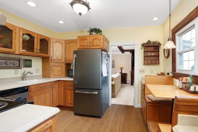 kitchen featuring appliances with stainless steel finishes, glass insert cabinets, hanging light fixtures, light countertops, and light wood-style floors