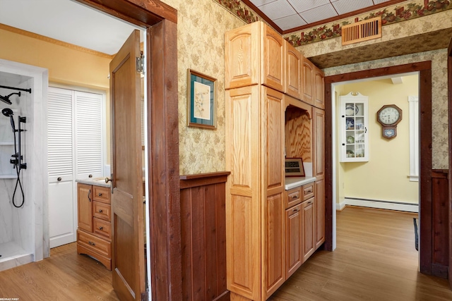 hall with a baseboard heating unit, light wood-style floors, visible vents, and wallpapered walls