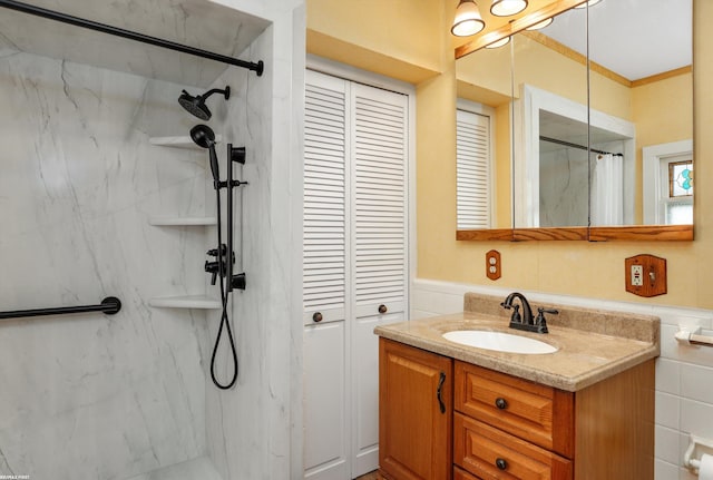 bathroom featuring a marble finish shower, wainscoting, ornamental molding, vanity, and a closet