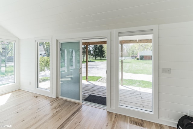 doorway with a wealth of natural light, vaulted ceiling, and light hardwood / wood-style floors