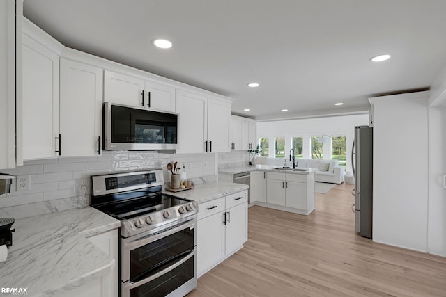 kitchen featuring stainless steel appliances, decorative backsplash, sink, light stone counters, and light wood-type flooring