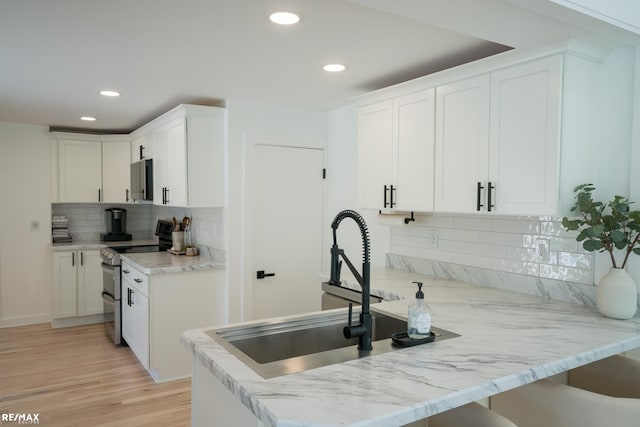 kitchen with light hardwood / wood-style flooring, decorative backsplash, white cabinetry, light stone countertops, and stainless steel electric stove