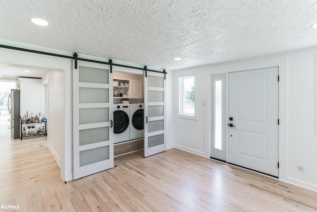 entryway with washer and dryer, a textured ceiling, light hardwood / wood-style floors, and a barn door