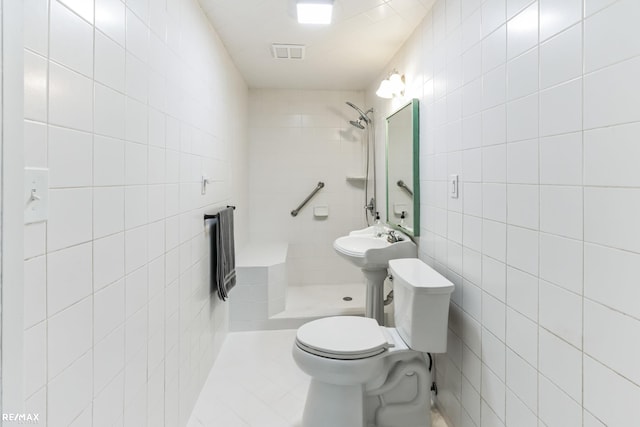 bathroom featuring tiled shower, toilet, tile patterned floors, and tile walls