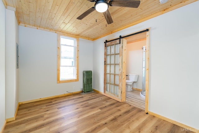 spare room featuring wood ceiling, light hardwood / wood-style flooring, ceiling fan, radiator, and a barn door