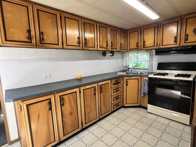 kitchen featuring under cabinet range hood, a sink, brown cabinetry, dark countertops, and gas range