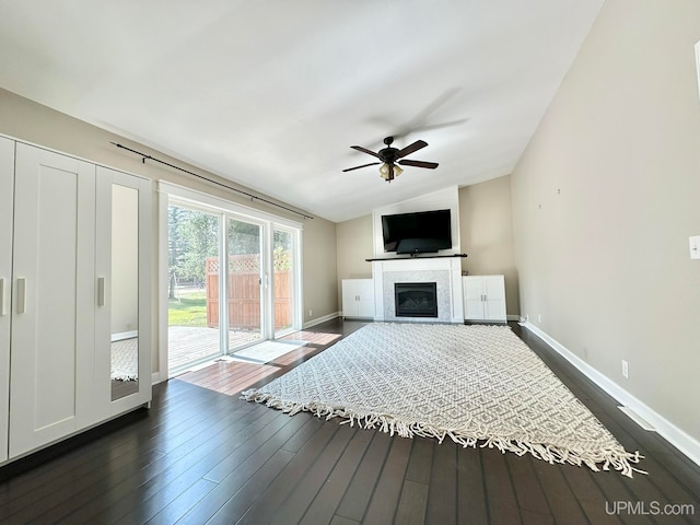 unfurnished living room with ceiling fan, dark hardwood / wood-style floors, lofted ceiling, and a tiled fireplace