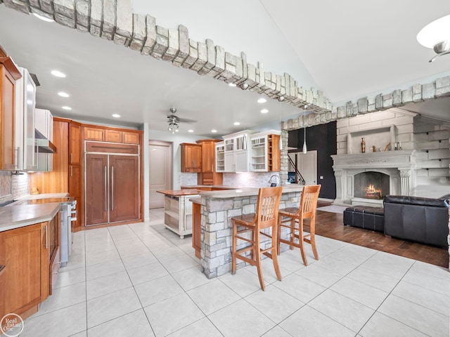 kitchen with backsplash, a kitchen bar, paneled built in refrigerator, wall chimney range hood, and ceiling fan