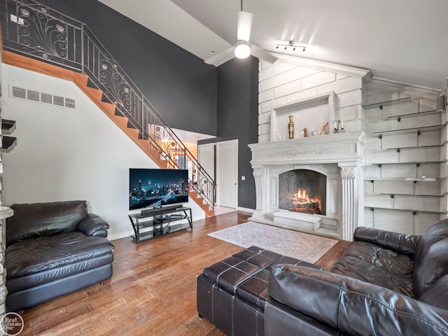 living room with ceiling fan, a large fireplace, a towering ceiling, and wood-type flooring