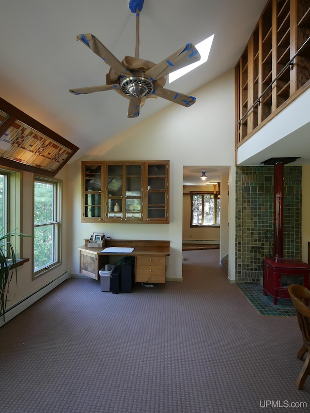 interior space with a skylight, a wood stove, high vaulted ceiling, ceiling fan, and dark carpet