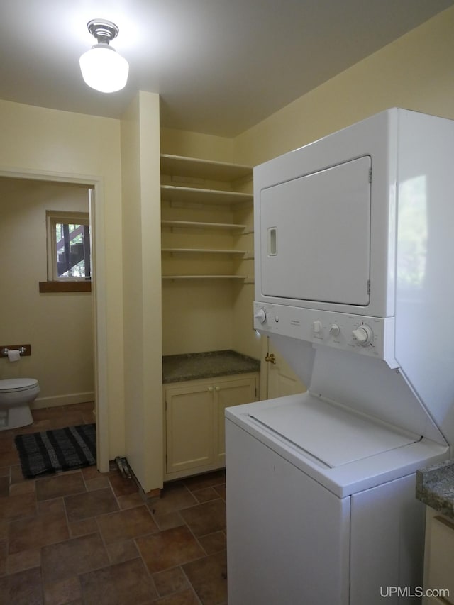 washroom with stacked washer / drying machine and dark tile patterned flooring