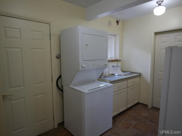 laundry area with sink, dark tile patterned flooring, cabinets, and stacked washer and clothes dryer