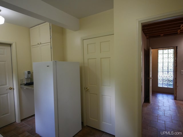 kitchen featuring beam ceiling, dark tile patterned flooring, white refrigerator, and white cabinets