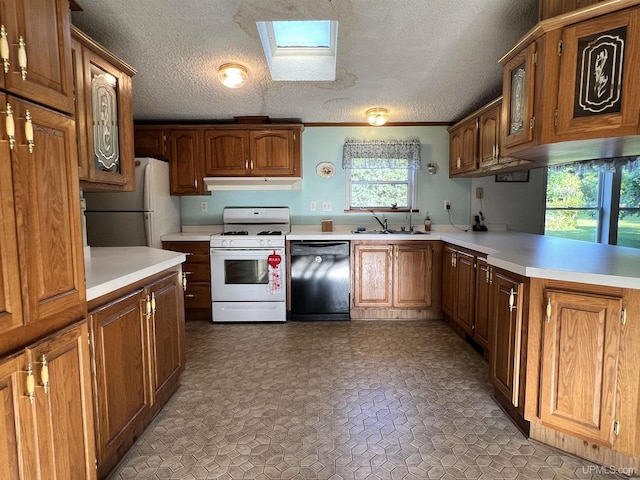 kitchen with a skylight, light countertops, a sink, white appliances, and under cabinet range hood