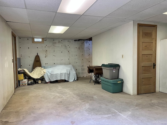 bedroom with concrete block wall, unfinished concrete floors, and a paneled ceiling