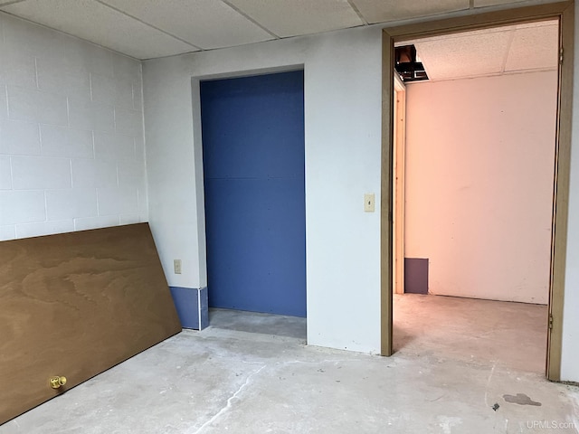 unfurnished room with a paneled ceiling, unfinished concrete flooring, and concrete block wall