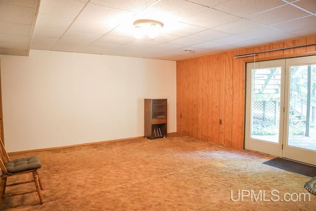 carpeted spare room with a wealth of natural light, wooden walls, and a paneled ceiling