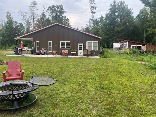 rear view of property with a lawn, a storage shed, an outdoor fire pit, and a patio area