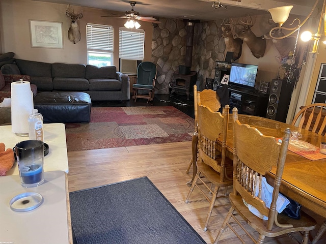 dining space with ceiling fan with notable chandelier, hardwood / wood-style flooring, and a wood stove