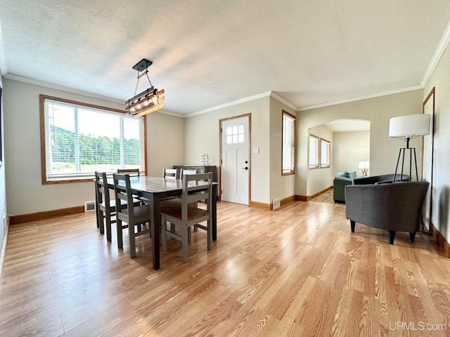 dining room with a textured ceiling, ornamental molding, and light wood-type flooring