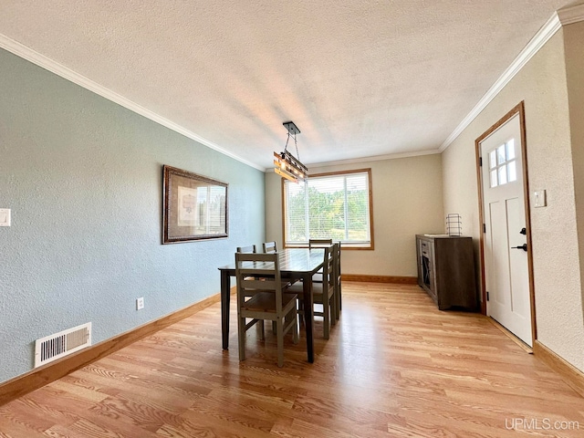 dining space with a textured ceiling, crown molding, and light hardwood / wood-style floors