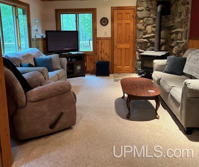 carpeted living room with a wood stove, wooden walls, and wainscoting