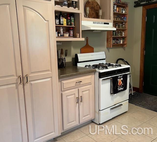 kitchen featuring white range with gas stovetop, light tile patterned floors, under cabinet range hood, and open shelves