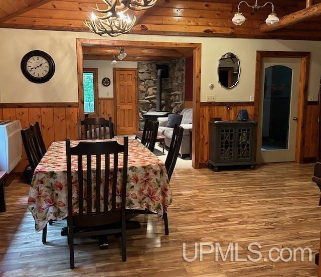 dining room with a wood stove, a wainscoted wall, a notable chandelier, and wood finished floors