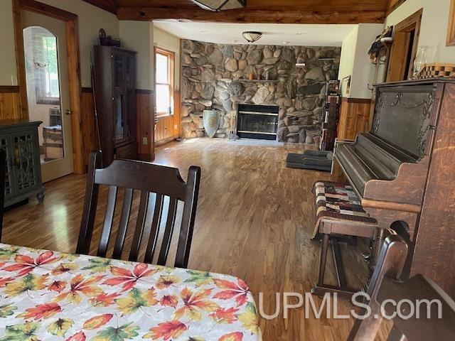 living area with wooden walls, a wainscoted wall, wood finished floors, a fireplace, and beam ceiling