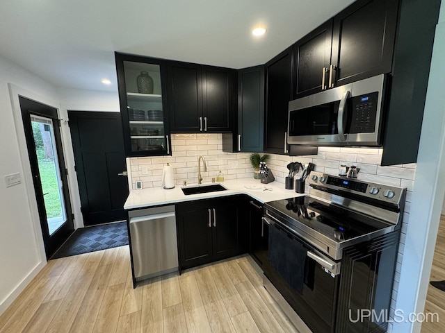 kitchen featuring light countertops, dark cabinetry, a sink, light wood-style floors, and appliances with stainless steel finishes