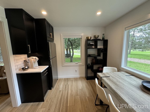 kitchen with light countertops, light wood finished floors, a wealth of natural light, freestanding refrigerator, and dark cabinets