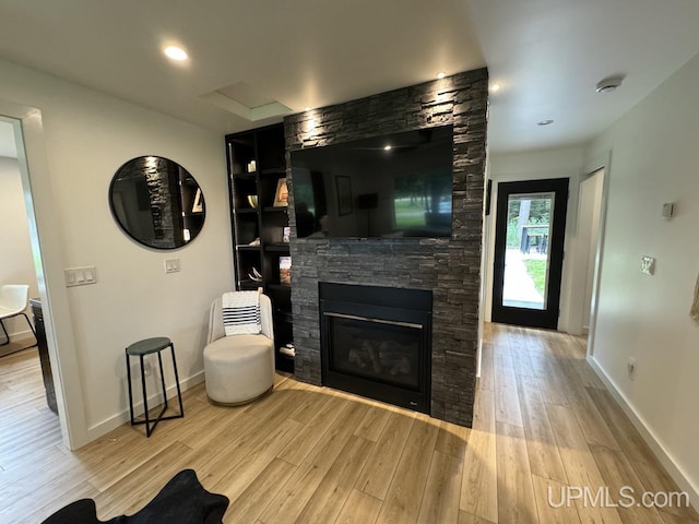 living area featuring a stone fireplace, baseboards, and wood finished floors