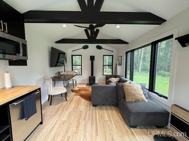 living room with vaulted ceiling with beams, a wood stove, a ceiling fan, and light wood finished floors
