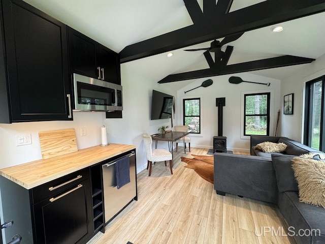kitchen featuring open floor plan, a wood stove, dark cabinetry, lofted ceiling with beams, and stainless steel appliances