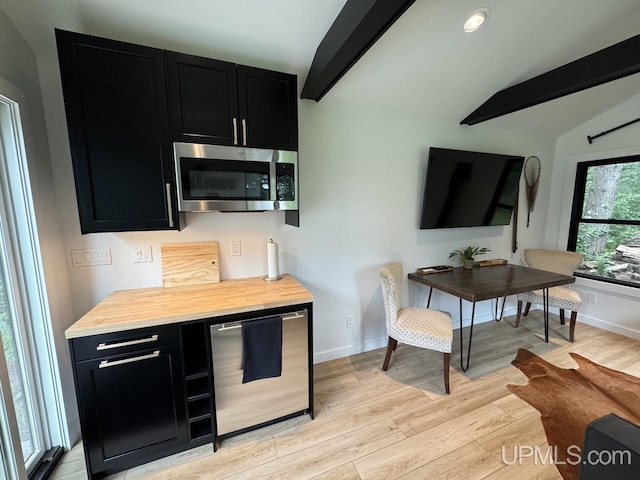 kitchen with vaulted ceiling with beams, light wood-style flooring, dark cabinets, and stainless steel appliances