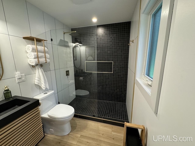 full bath featuring toilet, a tile shower, vanity, and wood finished floors