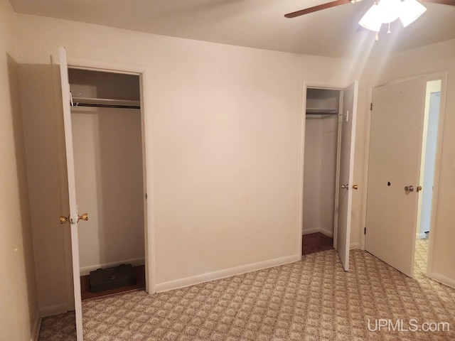 unfurnished bedroom with ceiling fan, light carpet, and two closets