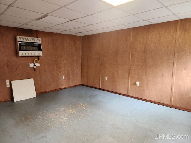 unfurnished room featuring heating unit, wooden walls, and a drop ceiling