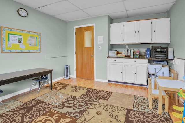 kitchen featuring light wood-type flooring, white cabinetry, and a drop ceiling